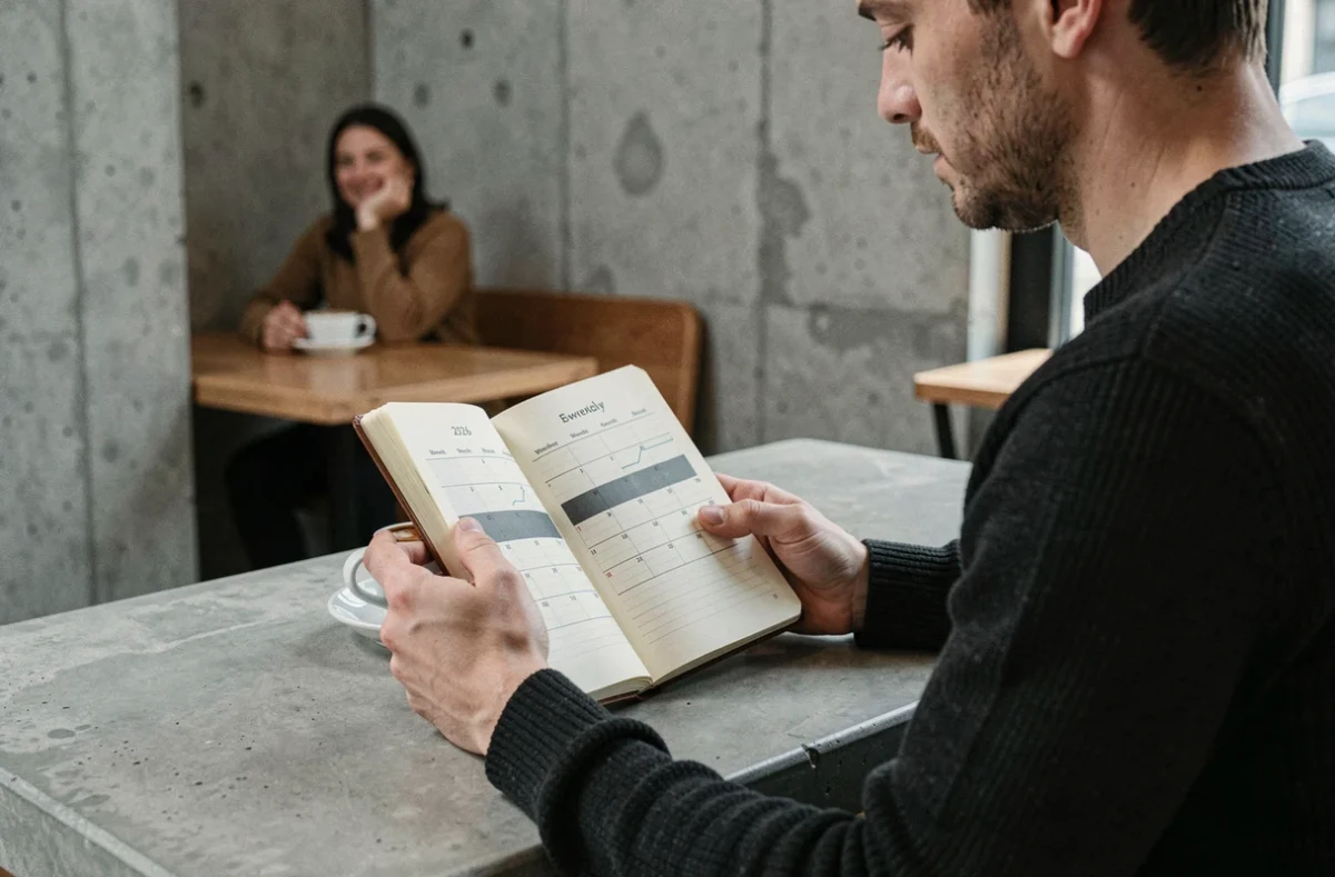 Homme consultant son bullet journal avec un calendrier 2026 semaines paires et impaires dans un café minimaliste au décor en béton