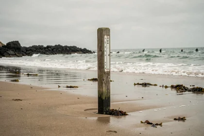 Repère de marée planté dans le sable humide d'une plage d'Anglet avec l'océan Atlantique en arrière-plan